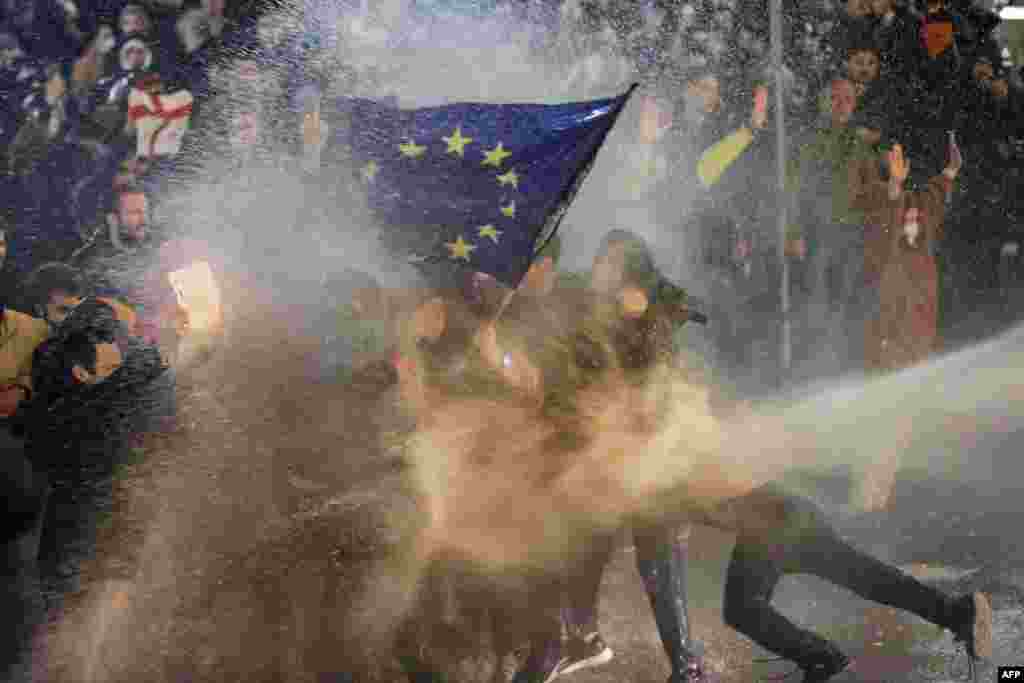 Ýewropa Bileleşiginiň baýdagyny göterýän demonstrantlara suw sepilýär. Protestçileriň we polisiýanyň arasynda çaknyşyklar 2023-nji ýylyň&nbsp;7-nji martynda Tbiliside Gürjüstanyň mejlisiniň golaýynda boldy. Gürji polisiýasy paýtagt Tbiliside jedelli &quot;daşary ýurt agentleri&quot; kanunyna garşylyk bildirmek üçin köçä çykan müňlerçe adamlyk protestiň gatnaşyjylaryna garşy gözi ýaşardýan gazy we suw pürkýän gurallary ulandy. (AFP suraty)