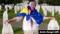 A Bosnian Muslim woman mourns next to the graves of her children and husband at the Srebrenica Memorial Center in Potocari.