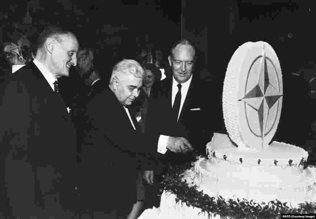 NATO Secretary-General Manlio Brosio (left) and U.S. Secretary of State William Rogers watch Icelandic Prime Minister Bjarni Benediktsson cut a NATO-themed cake during celebrations of the alliance’s 20th anniversary in Washington D.C. in 1969.