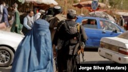 Taliban forces on patrol in Kabul with a woman in a burqa in the foreground.